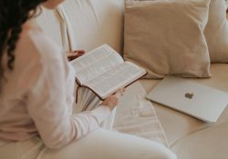 Woman reading a book on a cozy sofa with a laptop nearby. Ideal for lifestyle and relaxation themes.